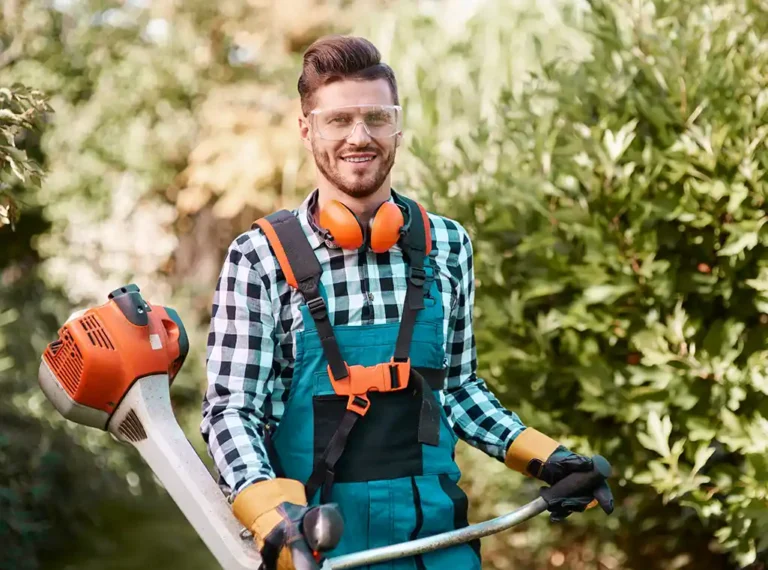 Mann in Latzhose, Ohrschützer und Motorgrassense arbeitet im Garten